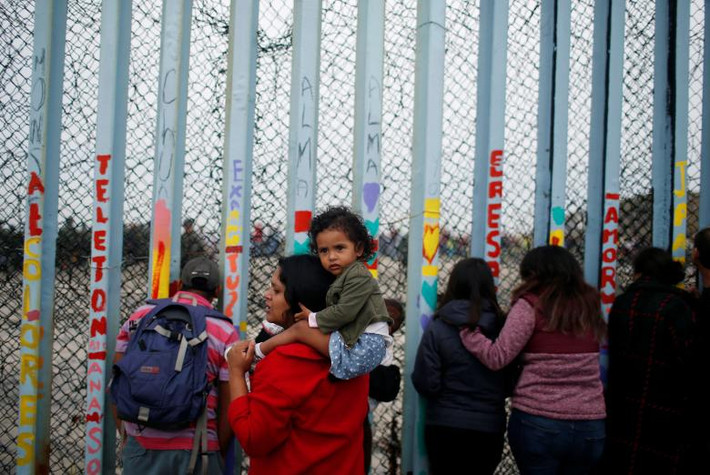 Một nhóm người di cư đứng bên kia hàng rào biên giới Mỹ-Mexico ở Tijuana, Mexico, nhìn về phía đoàn người biểu tình ở San Diago, Mỹ.