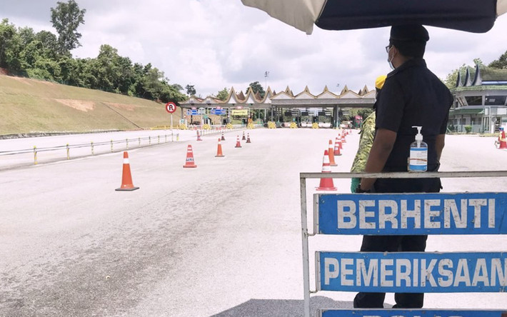 Cảnh sát đứng gác tại chốt chặn nhìn ra con đường không một bóng người ở Neggeri Sembilan, Malaysia. Ảnh: Bernama.