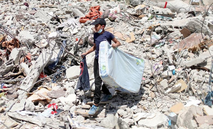 Một bé trai Palestine mang tấm đệm đi qua đống đổ nát ở thành phố Gaza ngày 2/6.