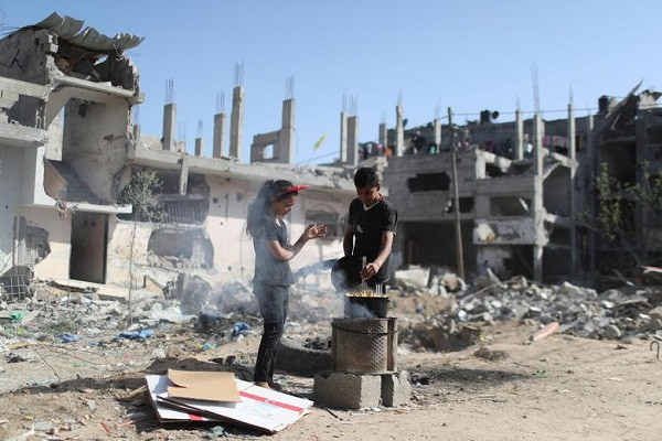 Một bé trai Palestine luộc ngô ngoài trời, gần đống đổ nát của những ngôi nhà bị phá hủy trong cuộc không kích của Israel - Palestine, tại Gaza ngày 9/6.