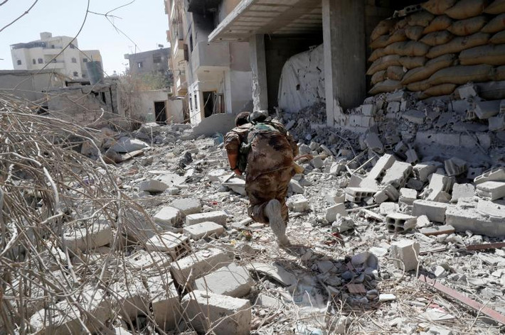Một thành viên của Lực lượng Dân chủ Syria (SDF) tìm nơi ẩn nấp trong cuộc giao tranh với IS gần sân vận động ở Raqqa, Syria, ngày 4/10. Ảnh: Reuters.