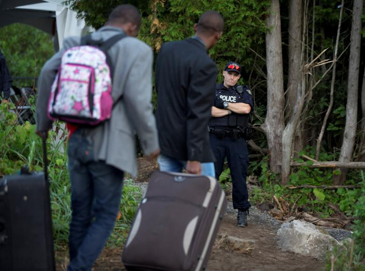 Một cảnh sát Canada đứng quan sát khi các di dân Haiti tìm cách vượt biên vào Canada từ đường Roxham ở Champlain, thành phố New York (Mỹ). Khi ở Canada, họ sẽ bị bắt và thẩm vấn cũng như kiểm tra an ninh trước khi được phép nộp đơn xin tị nạn.