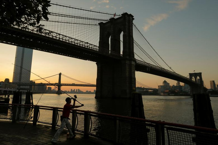 Người đàn ông câu cá dưới cây cầu Brooklyn ở New York lúc mặt trời mọc ngày 21/7.