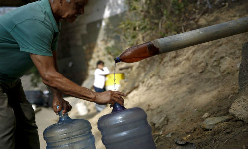 Một người đàn ông lấy nước vào bình cạnh đường cao tốc dọc núi Avila ở Caracas, Venezuela, ngày 3/3/2016.
