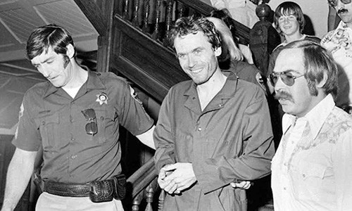 Ted Bundy là kẻ giết người hàng loạt, đã tấn công và sát hại nhiều phụ nữ trong những năm 1970. Trong ảnh, dù đang bị còng tay và áp giải, Ted vẫn cười tươi trước ống kính. Ảnh: The Richest.
