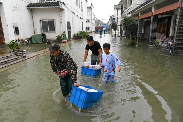 Người dân địa phương mang theo đồ đạc đi qua con đường ngập nước gần Hồ Sào, Hợp Phì, tỉnh An Huy, ngày 19/7. Theo Tân Hoa Xã, cảnh báo đỏ đã được ban bố tại các tỉnh An Huy và Giang Tây khi mưa lũ vẫn tiếp diễn.