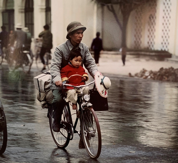 Em bé ngồi ngoan ngoãn phía trước trong khi bố đạp xe và chở theo nhiều đồ đạc phía sau.