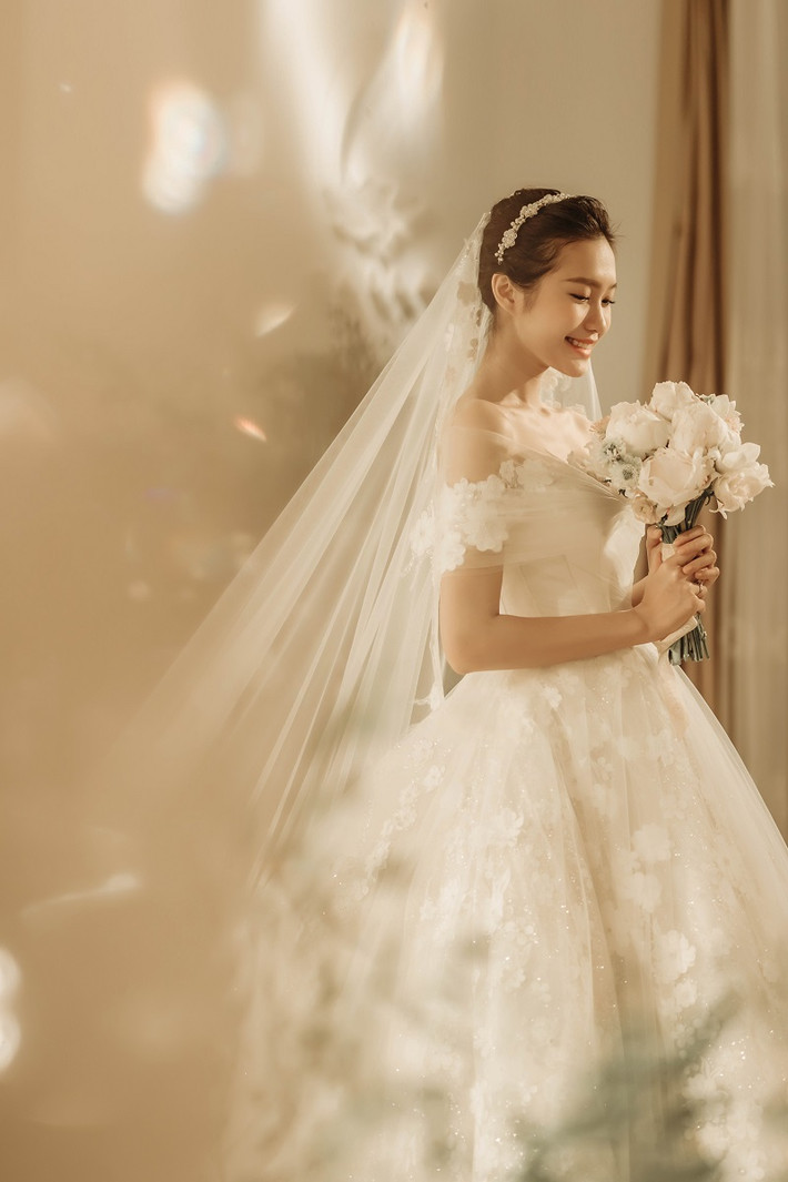 Bộ váy phủ ren với những bông hoa ngọt ngào yêu kiều, cộng thêm khăn voan mềm mại, nhìn cô dâu gốc Hà Nội càng thêm e ấp, duyên dáng tựa nàng công chúa bước ra từ truyện cổ tích để sánh bước cùng chàng hoàng tử của cuộc đời.