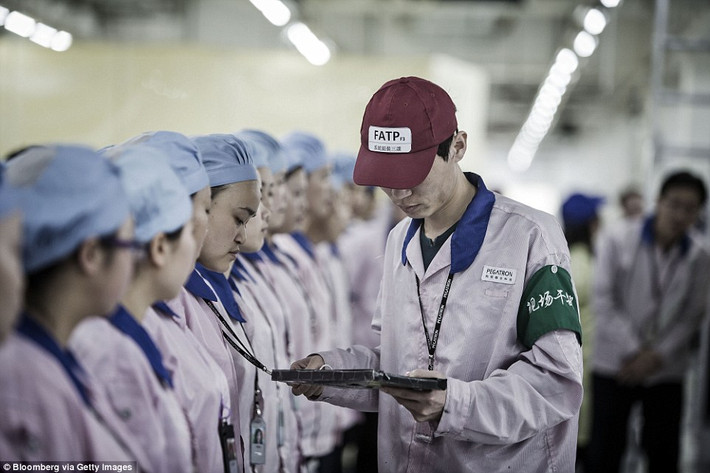 Các nhân viên nhà máy mặc bộ đồng phục hồng, đội mũ trùm màu xanh và đi dép cao su.