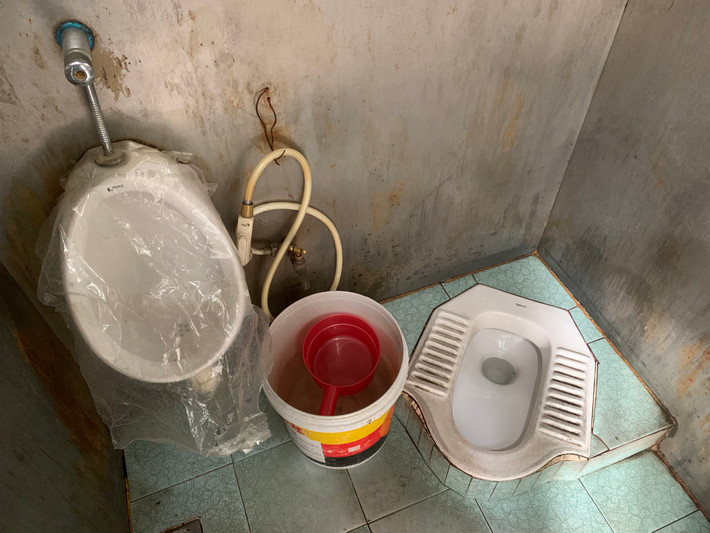 Phía trong nhà vệ là không gian chật trội, hạ tầng xuống cấp, bồn tiểu nam bị bọc kín túi nilon không cho sử dụng, hệ thống nước không có, phải múc nước sẵn trong chậu xối...