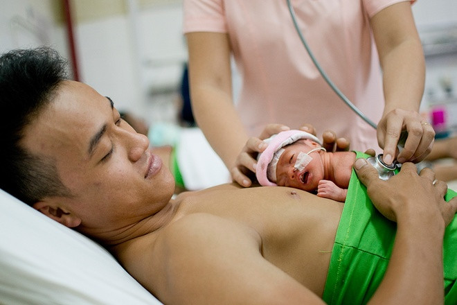 Dành thời gian cho vợ nghỉ ngơi, anh chồng thay vợ da tiếp da với con mới sinh trong phòng bệnh. Ảnh: Zing.