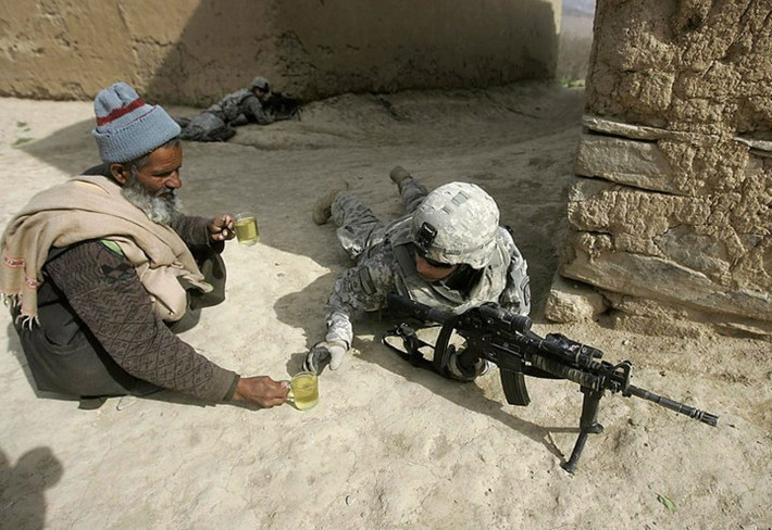 Một người đàn ông Afghanistan mang cốc nước cho người lính đang làm nhiệm vụ.