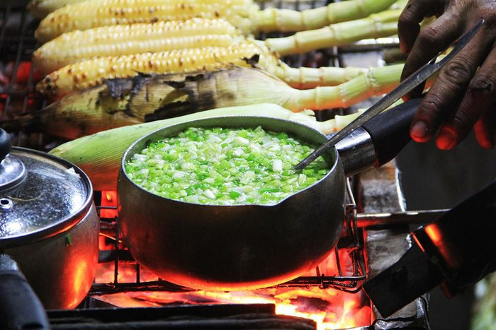 Bắp nướng mỡ hành: Những bắp ngô nướng vàng ươm nằm trên vỉ, có chút xém xém trên bề mặt, cô bán hàng cứ chốc lại lật lên và quét một lượt mỡ hành rồi lại lật xuống. Cái mùi thơm ngon, béo ngậy cứ kéo bạn “sà xuống” vào một hàng quán ngay lập tức.