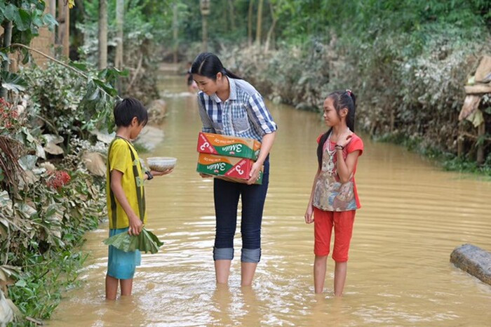 Hoa hậu Ngọc Hân không ngại lội nước, quần xắn ống cao trao lương thực cho các em nhỏ.