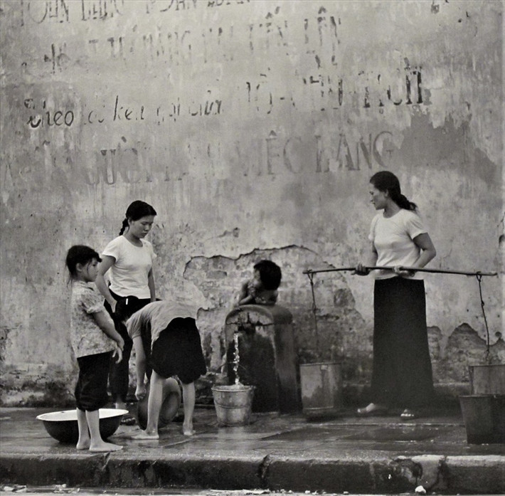 "Hà Nội 1967 - 1975" là triển lãm thứ 3 của nhiếp ảnh gia Thomas ở Việt Nam sau triển lãm năm 1972 và một buổi trình diễn cho dự án làm phim "Nước chanh đá cho Hong Li" năm 2000 trên Quảng trường Đông Kinh Nghĩa Thục ở Hà Nội. Trong ảnh là phụ nữ và các bé gái đi lấy nước để sử dụng trong sinh hoạt hàng ngày.