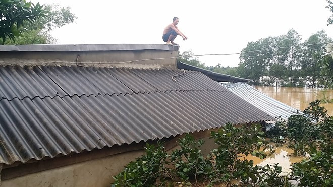 Một người đàn ông ở Hương Khê phải leo lên nóc nhà tránh lũ. Ảnh: Vietnamnet.