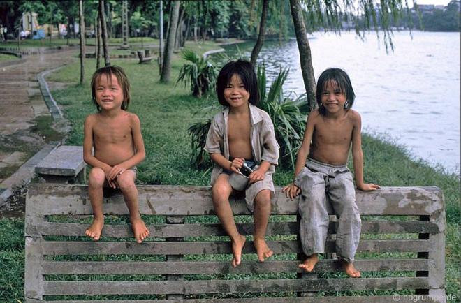 Ba trẻ em chơi đùa, cười tít mắt tại ghế đá bên hồ.