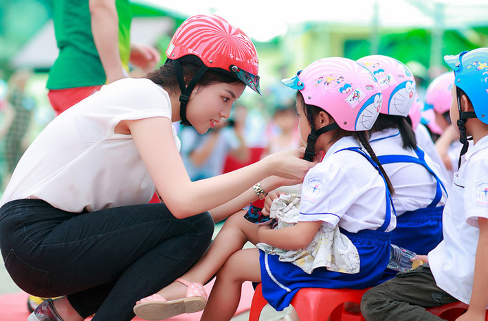 Sau đó, Hoa hậu Việt Nam 2014 xuống tận nơi giúp các em học sinh tiểu học cài mũ bảo hiểm.