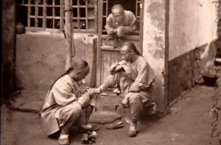 Thầy thuốc thăm khám chân cho một bệnh nhân. Nam giới Trung Quốc dưới thời nhà Thanh để tóc tết đuôi sam.