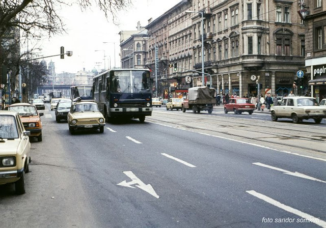 Đường phố Budapest đông đúc xe cộ. Hai bên đường là những tòa nhà văn phòng, cửa hàng tấp nập người đi lại.
