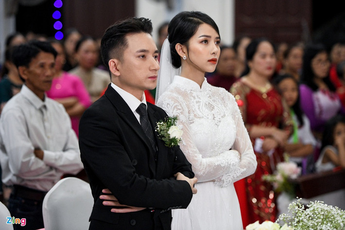 Trong thánh lễ hôn phối, nhạc sĩ Mắt biếc diện suit đen lịch lãm. Đứng cạnh anh, Huỳnh Khánh Vy mặc áo dài trắng được thiết kế tinh tế. Cả hai khoanh tay, thực hiện các nghi thức của buổi lễ.