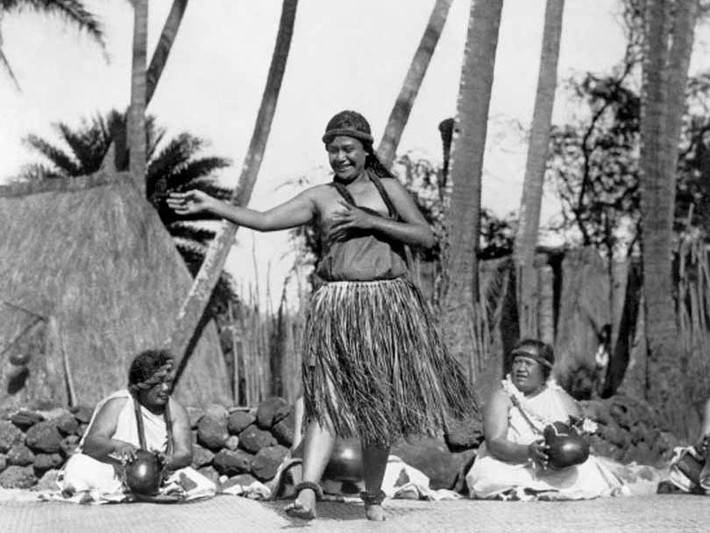 Năm 1924: Một vũ công người Hawai bản xứ nhảy múa trong khi những phụ nữ khác tạo nên nhịp điệu bằng nhạc cụ đặc biệt của họ. Ảnh: Getty.