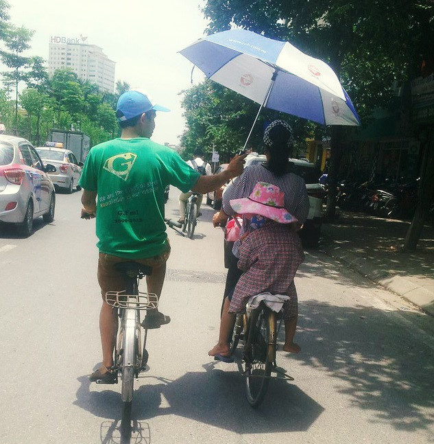Nhiệt độ ngoài trời lên tới 40 độ C, hình ảnh người chồng dùng ô che cho vợ và con gái trên đường thu hút sự chú ý của cộng đồng mạng. Bức ảnh do anh Minh Nhân chụp trên đoạn đường Văn Cao, quận Ba Đình, Hà Nội. Đây là một trong những cách chống nóng hài hước những ngày qua. Ảnh: Minh Nhân.