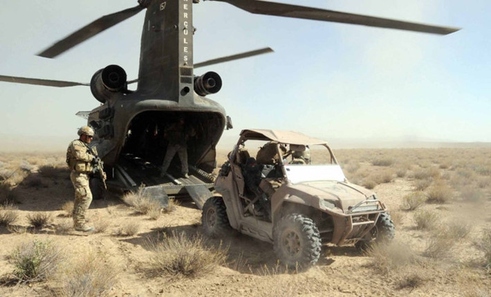 Một chiếc xe quân sự cùng các binh lính bước ra từ phía đuôi một chiếc trực thăng CH-47 Chinook.