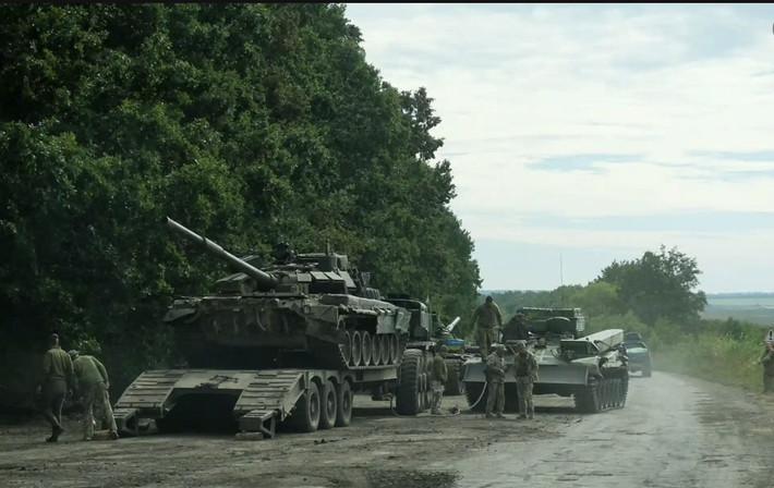 Binh lính Ukraine đang đưa một xe tăng Nga bị bỏ lại lên xe vận tải quân sự để di dời. Ảnh: The Guardian.
