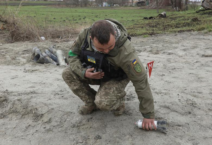 Lính đặc công Ukraine nhặt một phần chưa nổ của quả bom chùm còn sót lại gần làng Motyzhyn. Ảnh: Reuters.