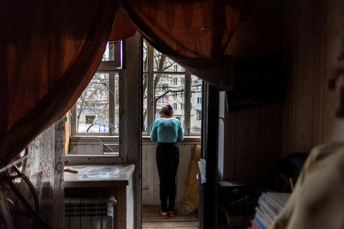 Cô gái tên Olena nhìn từ cửa sổ căn hộ bị hư hại do pháo kích ở Kharkiv, Ukraine, ngày 11/4.