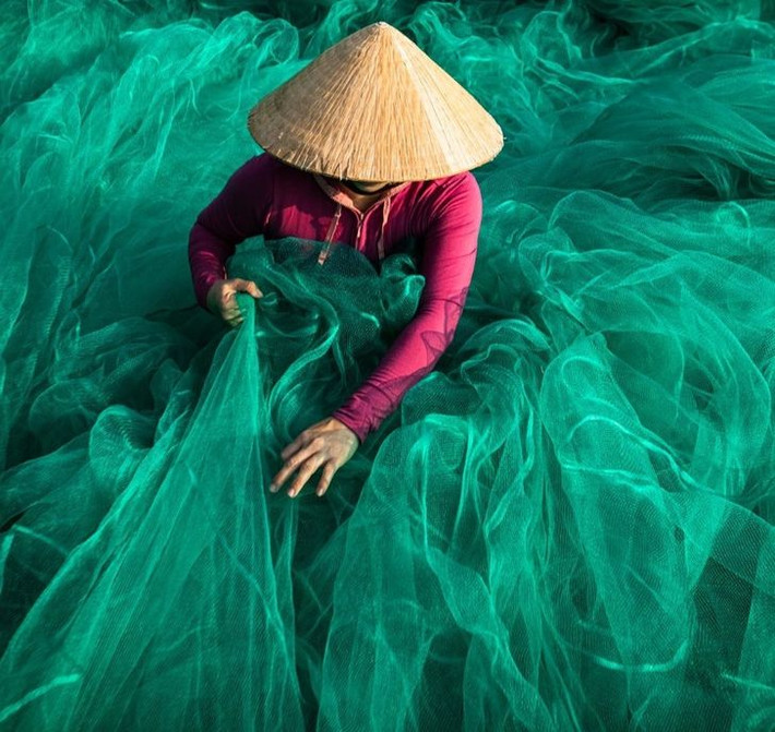 Một phụ nữ Việt Nam kiểm tra và sửa những chiếc lưới đánh bắt cá trước khi chúng được các ngư dân mang đi biển.