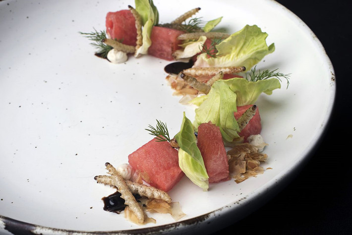 Món khai vị của nhà hàng gồm salad dưa hấu với kem bơ, thịt hun khói và sâu tre. Đầu bếp Mai Thitiwat tiết lộ những con sâu tre chiên giòn có mùi vị như mực. Chúng cũng là nguyên liệu đắt đỏ nhất, được nhập từ trang trại ở miền Bắc Thái Lan với giá 120 bath/kg (khoảng 81.000 đồng/kg). Ảnh: Bloomberg.