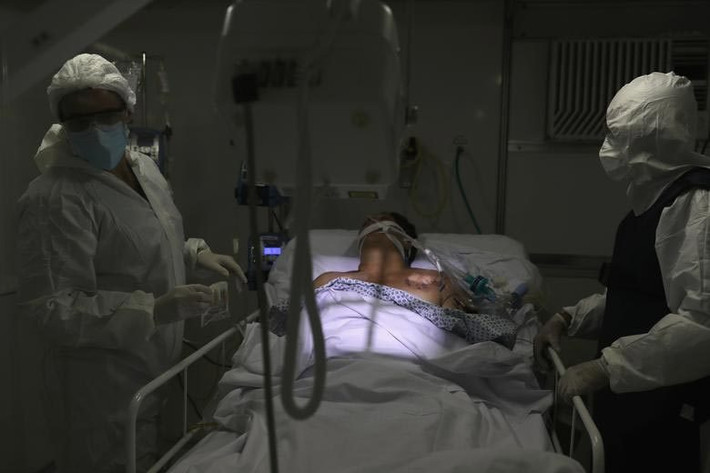 Hai bác sĩ mặc đồ bảo hộ kín mít đang chụp X-quang phổi cho bệnh nhân COVID-19 ở bệnh viện dã chiến tại Guarulhos, bang Sao Paulo, Brazil.