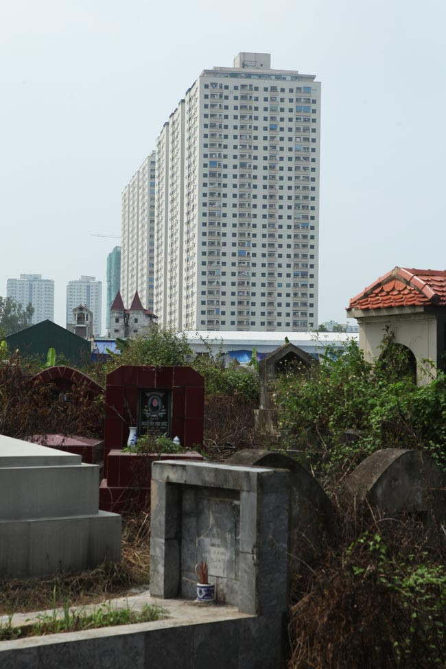 Những tòa nhà cao tầng, những khu đô thị cao cấp ở Hà Nội mọc lên bên cạnh, thậm chính ngay chính trên vùng đất trước đây từng là những nghĩa địa, bãi tha ma. Trong khi chưa thể di dời các nghĩa trang thì người sống chỉ còn biết sống chung với... người chết.