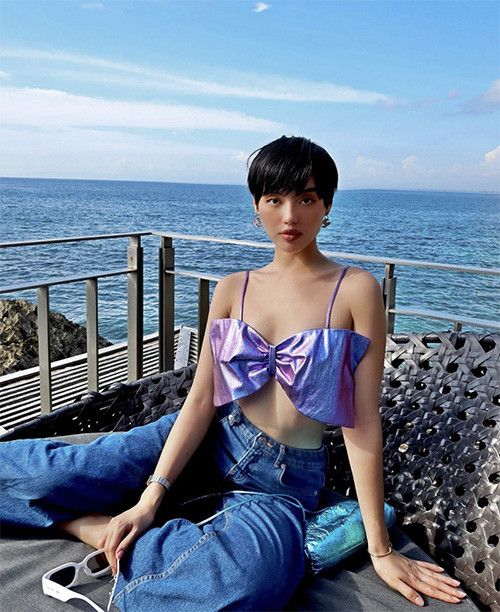 Khi đi du lịch biển, Khánh Linh lại chọn áo đính nơ kiểu hai dây để mix cùng quần jeans ống suông.