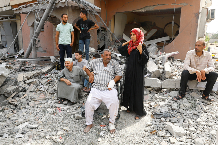 Người Palestine ngồi ngoài đường, nhìn lực lượng cứu hộ tìm kiếm thân nhân mất tích ở một tòa nhà đổ nát tại Khan Younis, miền nam Dải Gaza.