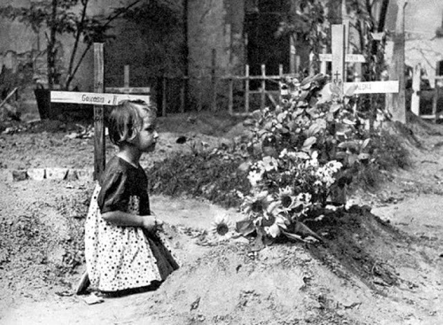 Bé gái quỳ trước ngôi mộ gần đường Mazowiecka, Warszawa, Ba Lan năm 1944. Nhiều trẻ em mất cha mẹ, người thân trong Chiến tranh thế giới 2 và trở thành những đứa trẻ mồ côi, không nơi nương tựa.