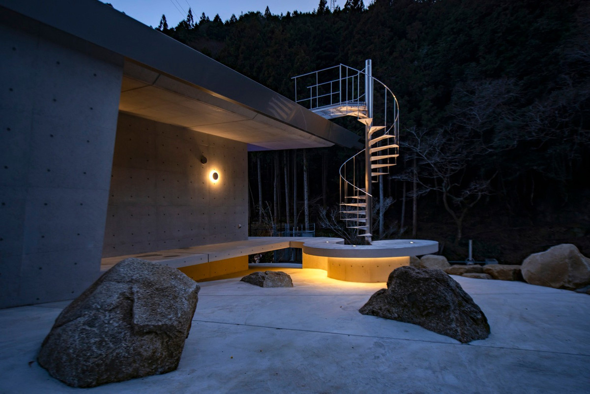 Sân lát đá, lối đi uốn cong ôm sát triền đồi, kết hợp các mảng bê tông mài và tường đá. Ảnh: T Architects Co.