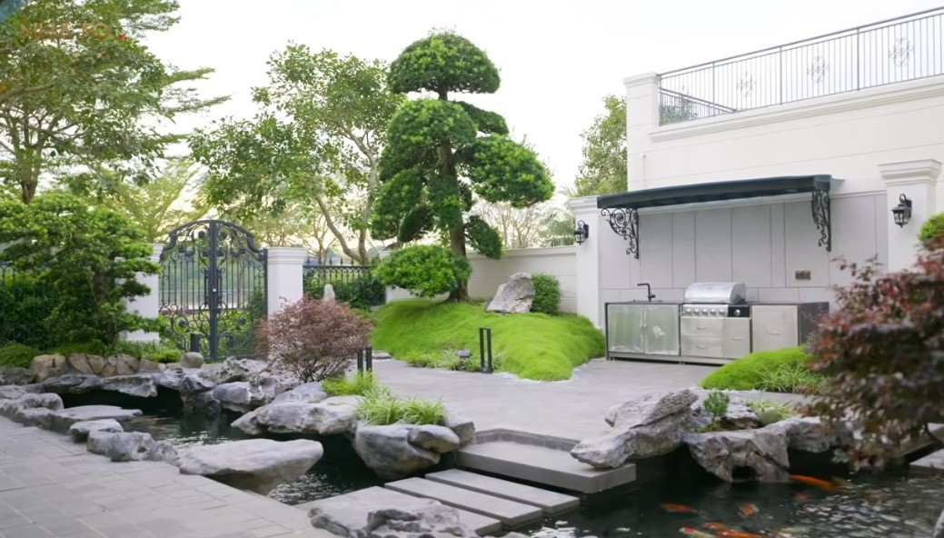 Không gian sân vườn đúng chất nghỉ dưỡng, có hồ cá, tiểu cảnh, cây xanh và khu vực bếp BBQ. Ảnh chụp màn hình