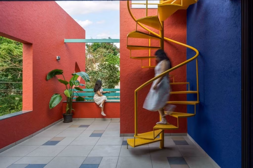 Cầu thang xoắn màu vàng nổi bật trên nền tường xanh - đỏ. Ảnh: Thearchitectsdiary