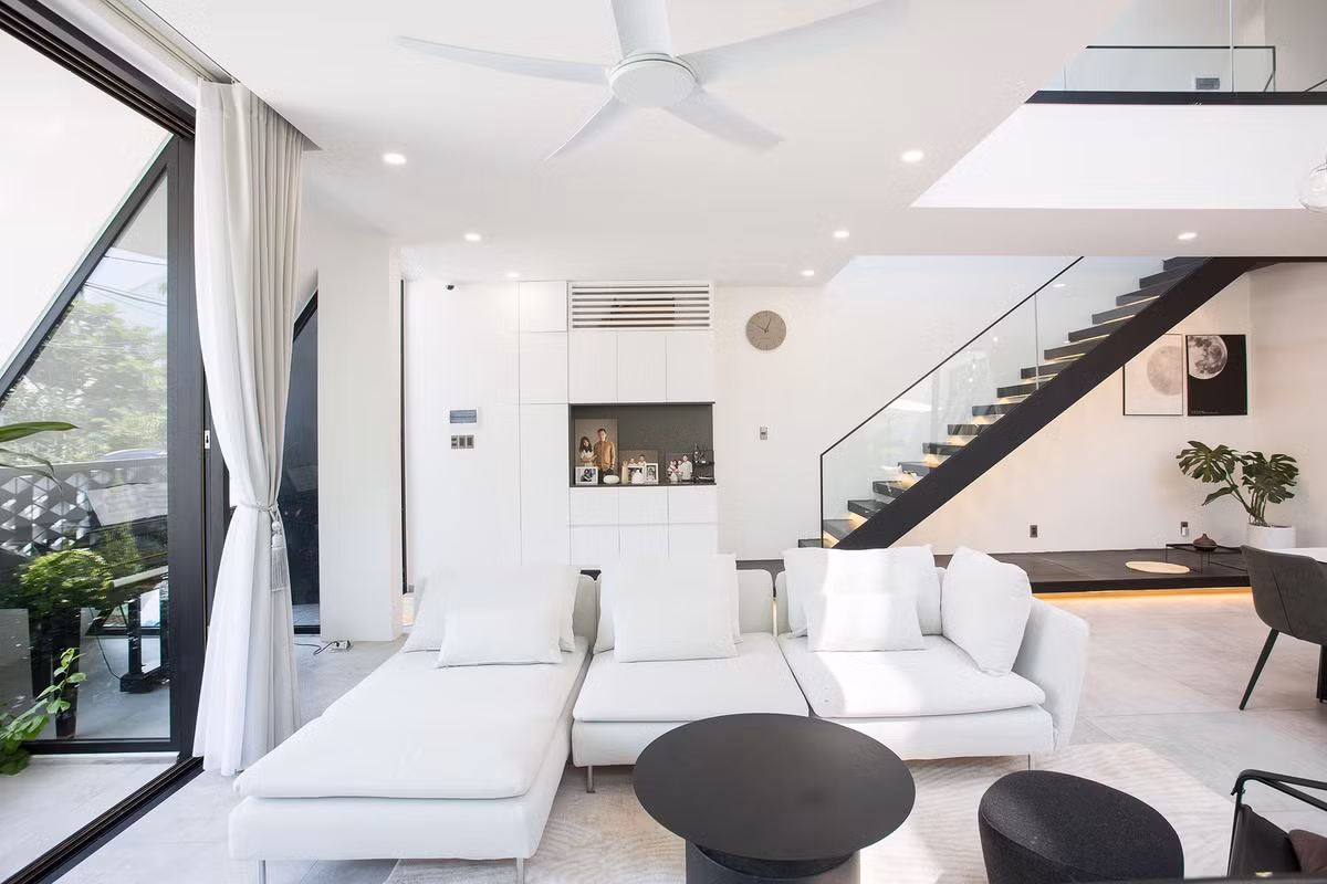 Phòng khách có sofa hình chữ L với gam màu trắng chủ đạo, kết hợp bàn trà màu nâu đen. Ảnh: Arch. Tô Hữu Dũng