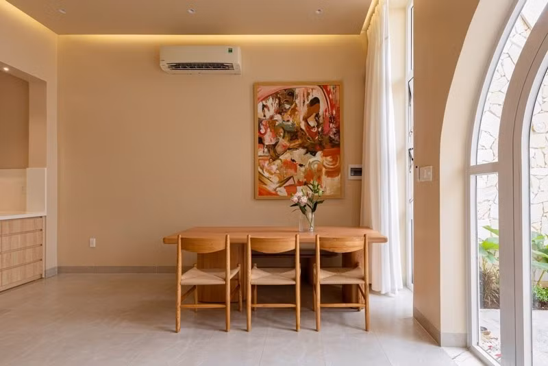 Phòng ăn ấm cúng với nội thất gỗ bo tròn, tranh trừu tượng và ánh sáng tự nhiên. Ảnh: Da Vàng studio