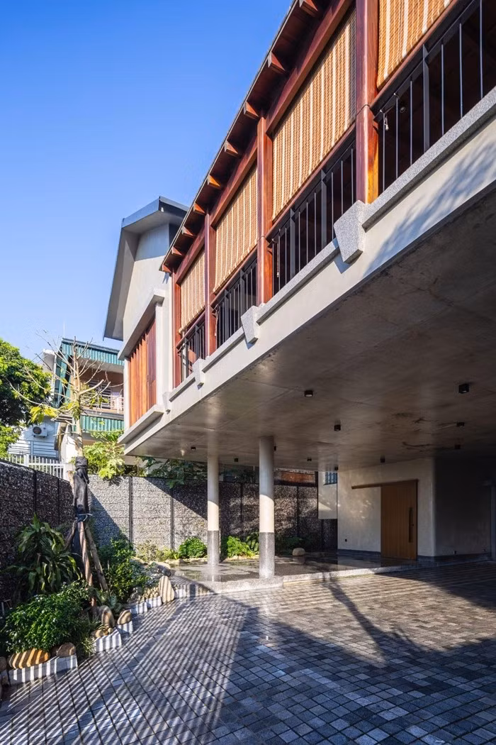 Mặt tiền tầng hai với hệ cửa chớp tre và lan can thép đơn giản. Lớp tường rọ đá và cổng đen mang lại cảm giác vững chãi. Ảnh: Trieu Chien