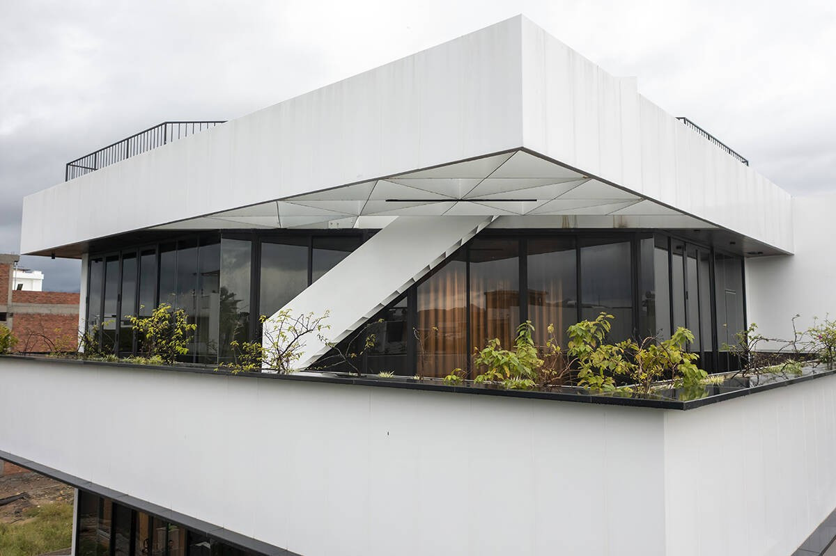 Lớp đệm không gian này giúp giảm bức xạ nhiệt, che mưa nắng, đồng thời kết hợp với lớp cây xanh trên mái giúp ngôi nhà tự "thở" mà không phụ thuộc hoàn toàn vào máy lạnh. Ảnh: A+ Architects