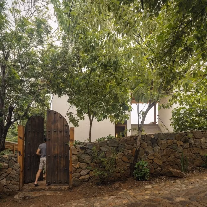 Lối vào nhà với cổng gỗ truyền thống và tường đá thô mộc. Ảnh: Archello