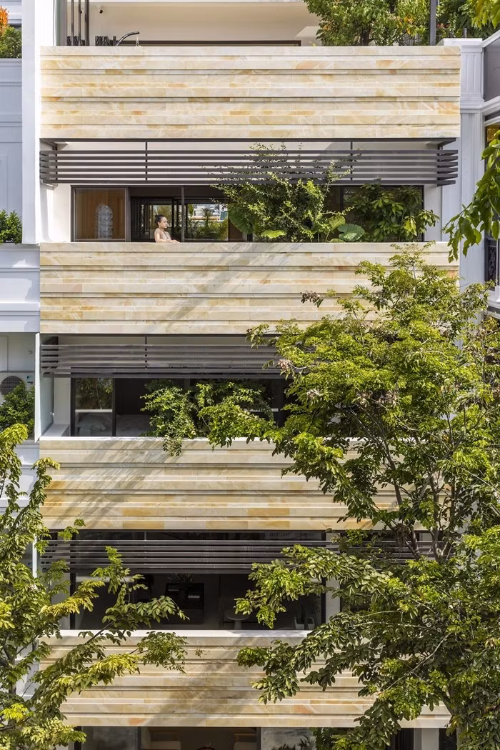 Mặt tiền sử dụng đá tự nhiên được chia nhỏ và xếp lớp theo phương ngang tạo hiệu ứng thẩm mỹ. Xen kẽ vào đó là hệ lam che nắng và mảng xanh được bố trí có chủ đích. Ảnh: Oki Hiroyuki