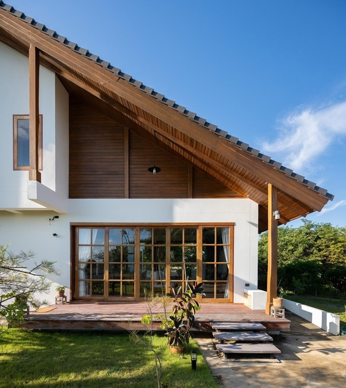 Mái dốc kết hợp trần hiên ốp gỗ tạo lớp vỏ mềm mại cho mặt tiền. Ảnh: Rungkit Charoenwat