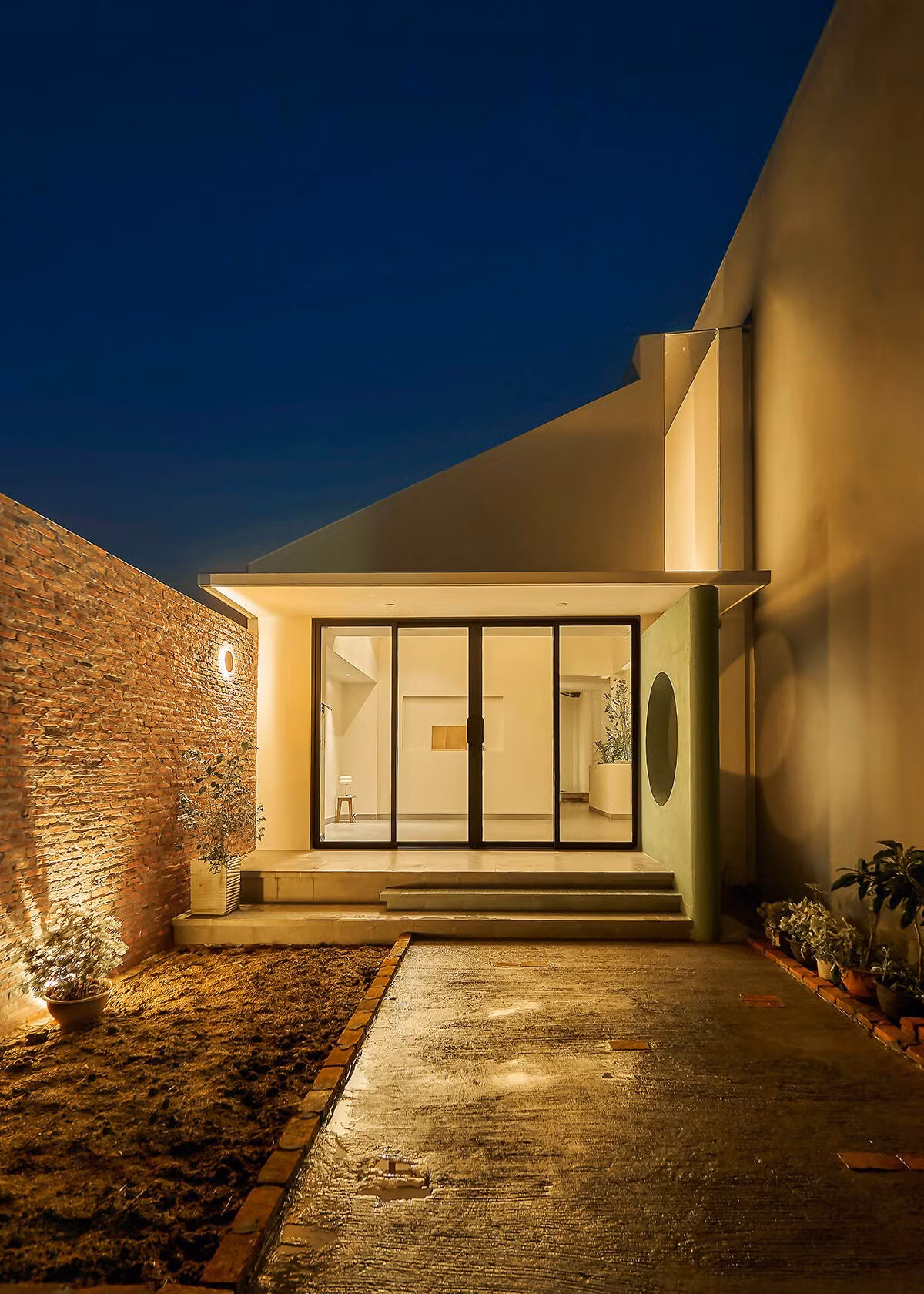 Đêm xuống, ánh sáng nội thất phản chiếu lên vách và mái kính, giúp ngôi nhà phát sáng nhẹ nhàng như một ngọn đèn trong khu phố. Ảnh: Nam Võ