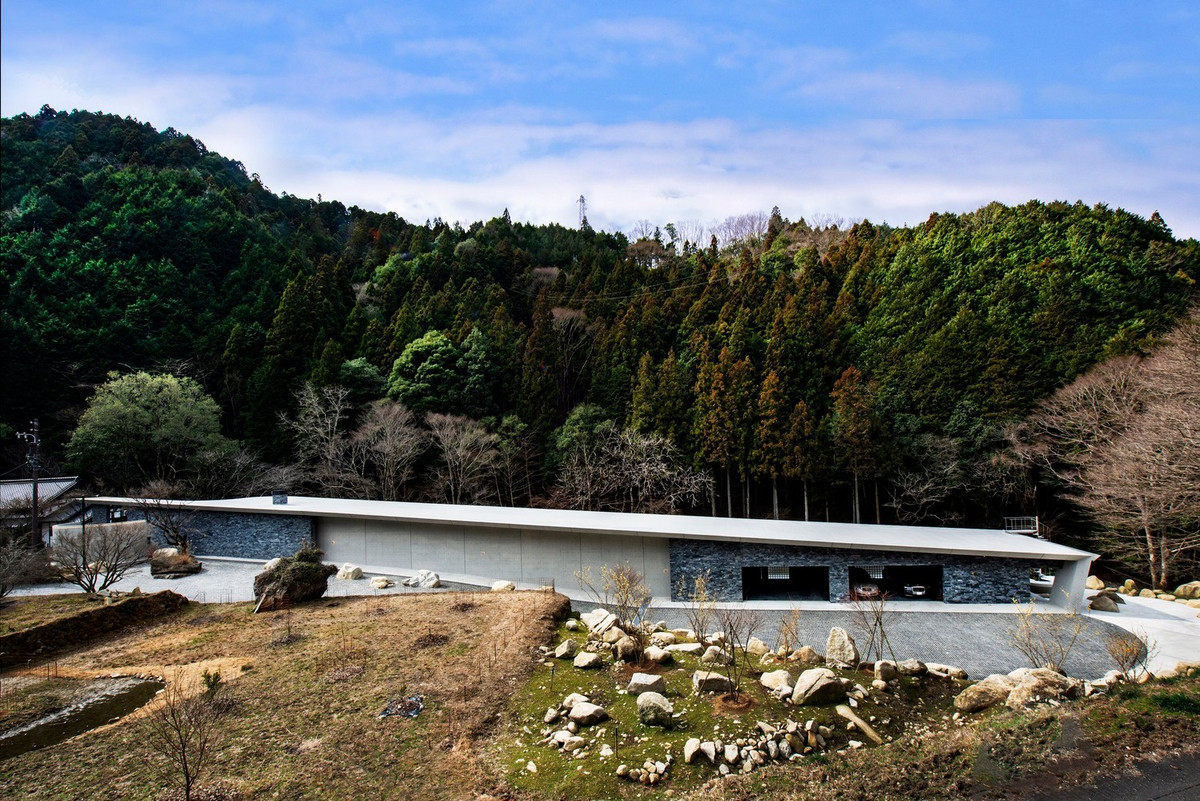 Sân lát đá, lối đi uốn cong ôm sát triền đồi, kết hợp các mảng bê tông mài và tường đá. Ảnh: T Architects Co.